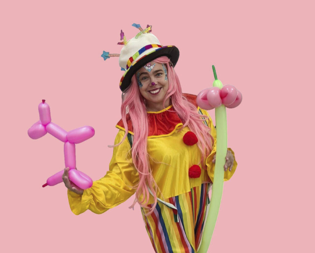 Pelle Nauru Nugetti poseeraa iloisesti värikkäissä vaatteissa ilmapallohahmot käsisään.