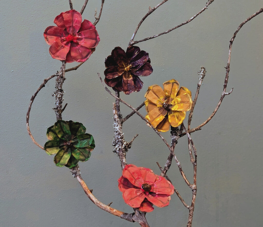 Askarreltu talventörröttäjä oksa, jossa luonno-oksaan kiinnitetty värikättäitä käpykukkia.